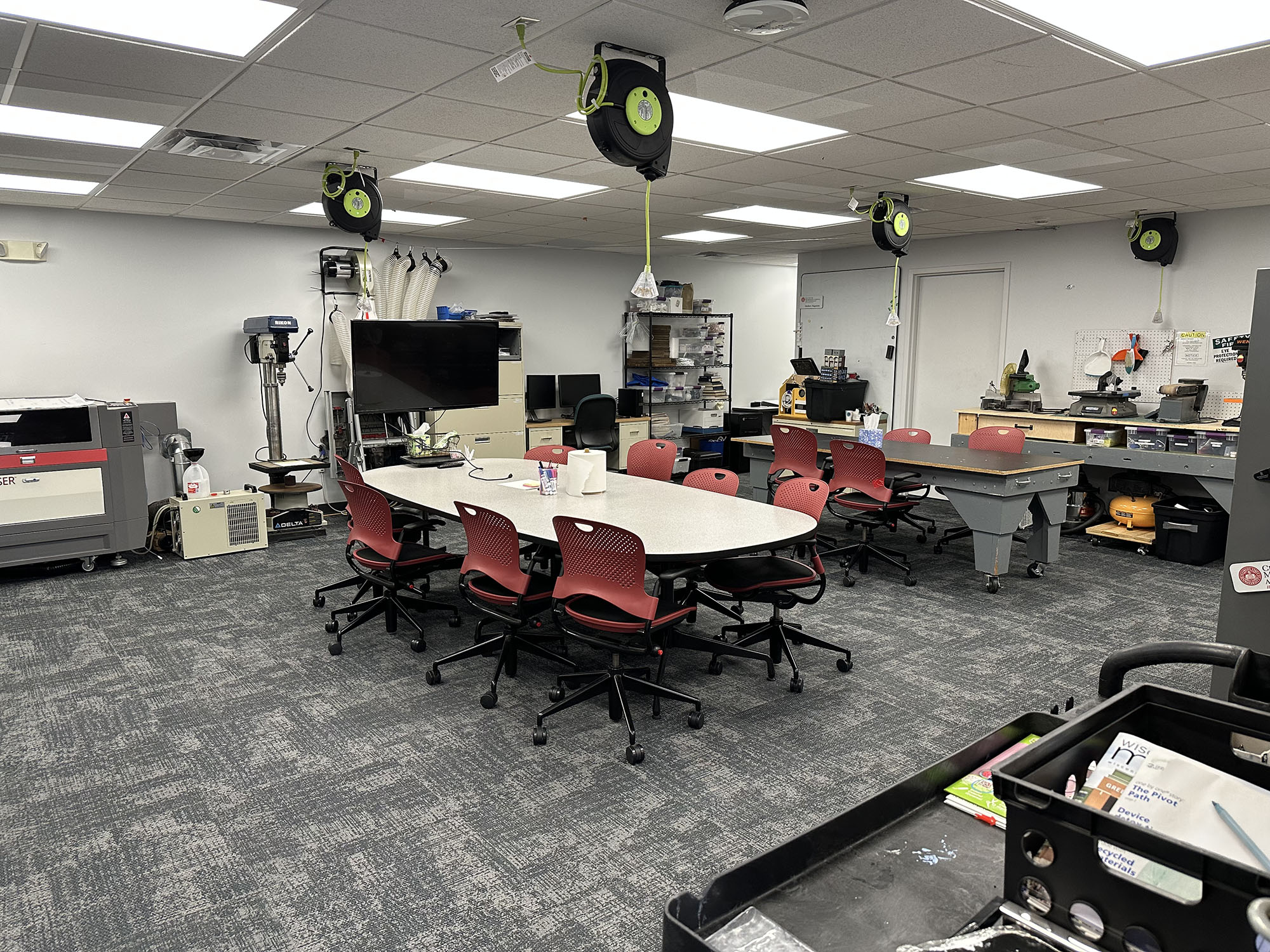 Photo of the STEM Hub conference table with a lab table behind and larger equipment and workspaces on the walls.